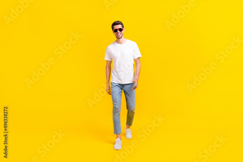 Full size photo of nice young brunet guy go wear spectacled t-shirt jeans sneakers isolated on yellow color background