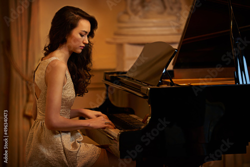 Its just her and the piano. Shot of a beautiful young woman playing the piano in an elegant room. photo