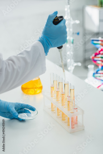 cropped view of geneticist with petri dish and micropipette near test tubes.