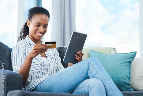 I cant say no to this. Shot of a young woman using a credit card and digital tablet at home.