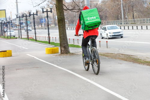 Courier with an isothermal green backpack on his back on a food delivery bike on a city street. © Sergii