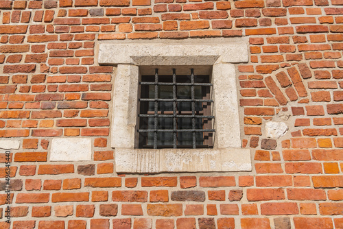 Window behind a wrought iron black metal grill on a red brick wall of a medieval building on a sunny day in Krakow