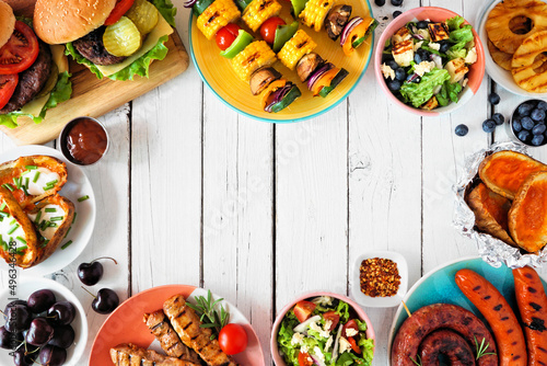 Summer BBQ or picnic food frame. Burgers, grilled meat, vegetables, fruits, salad and potatoes. Top view on a white wood background. Copy space.