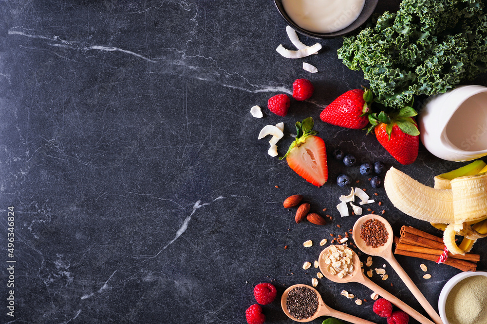 Healthy food side border. Smoothie making concept. Above view on a dark slate background. Copy space. Fruit, yogurt, almond milk and a variety of ingredients.