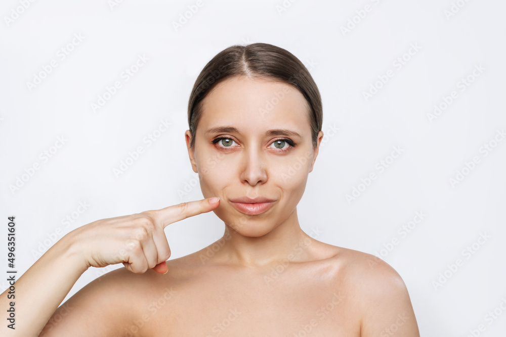 Portrait of young caucasian woman with lips after lip enhancement isolated on a white background. The girl demonstraes result of lip augmentation pointing at them with her finger. Injection of filler Portrait of young caucasian woman with lips after lip enhancement isolated on a white background. The girl demonstraes result of lip augmentation pointing at them with her finger. Injection of filler