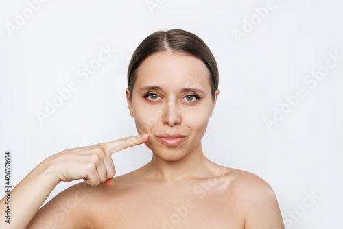 Portrait of young caucasian woman with lips after lip enhancement isolated on a white background. The girl demonstraes result of lip augmentation pointing at them with her finger. Injection of filler