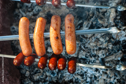 Smoked sausages are fried on a fire (on coals). Meat sausages on skewers. Cooking food while camping.