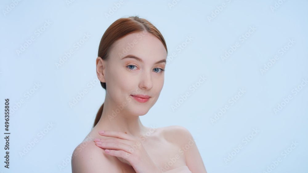 Young ginger woman touches her shoulder with pleasure against a blue background | Beauty model posing form skin care products commercial. Young ginger woman touches her shoulder with pleasure against a blue background | Beauty model posing form skin care products commercial.
