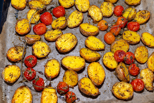 Baked potatoes and cherry tomatoes lying on a baking tray on the table.