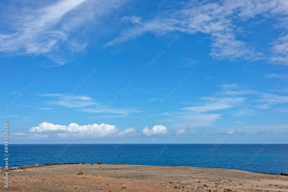 View of the blue sea and sky with cirrus clouds and white cumulus clouds near the horizon.