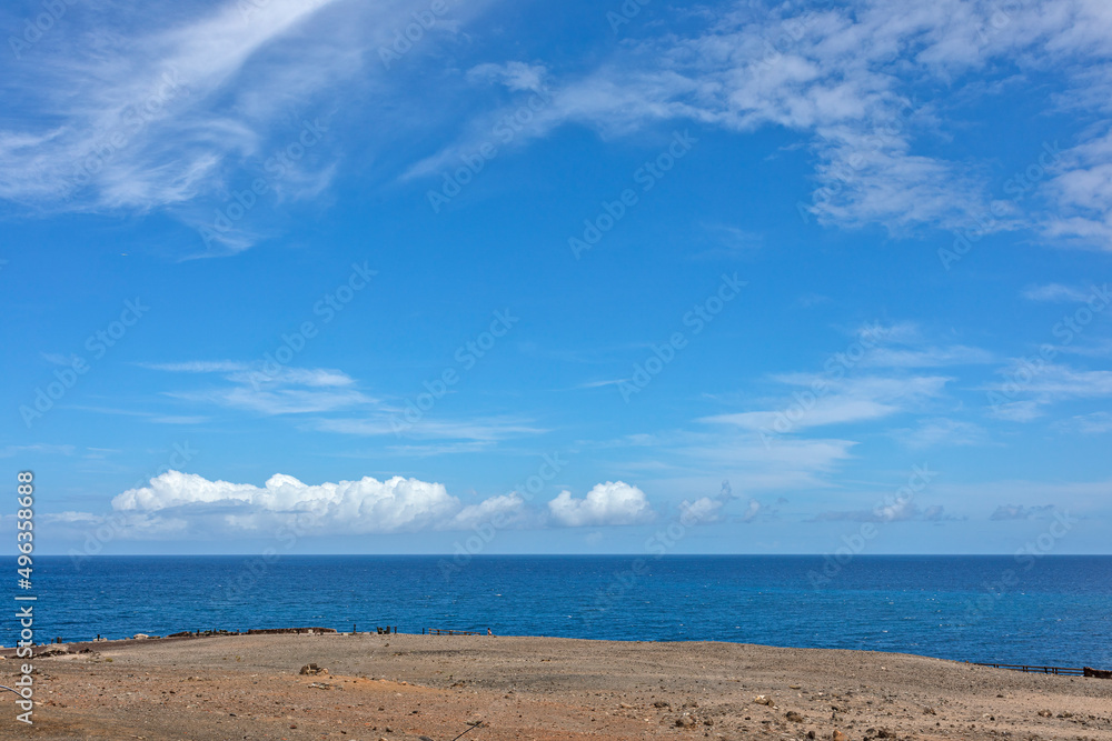 View of the blue sea and sky with cirrus clouds and white cumulus clouds near the horizon. View of the blue sea and sky with cirrus clouds and white cumulus clouds near the horizon.