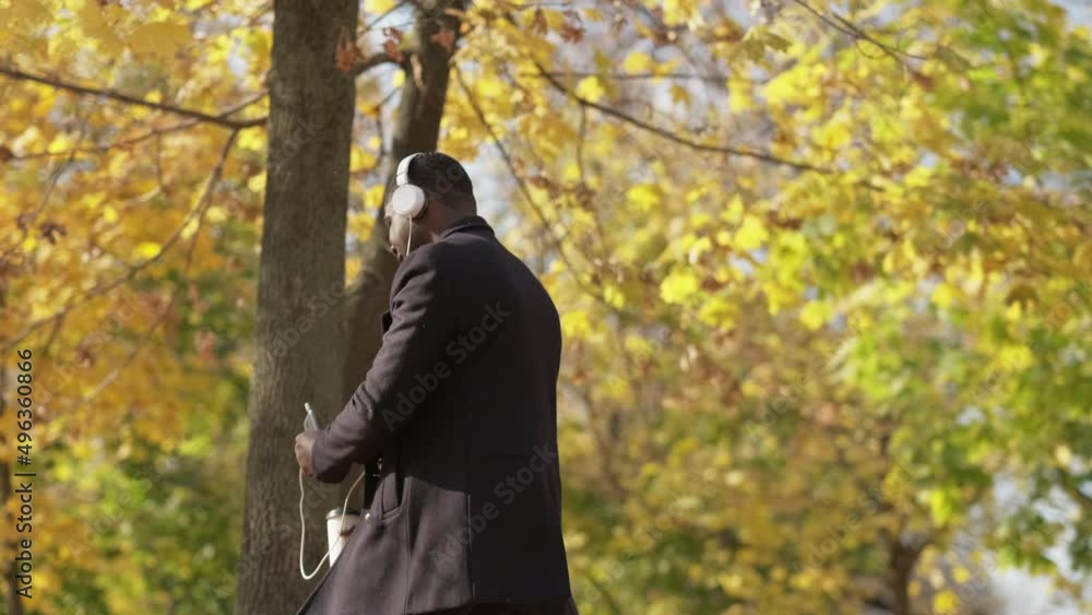 Music joy. Carefree mood. Outdoor fun. Overjoyed funny man listening favorite song in headphones on phone dancing with coffee at autumn park. Music joy. Carefree mood. Outdoor fun. Overjoyed funny man listening favorite song in headphones on phone dancing with coffee at autumn park.