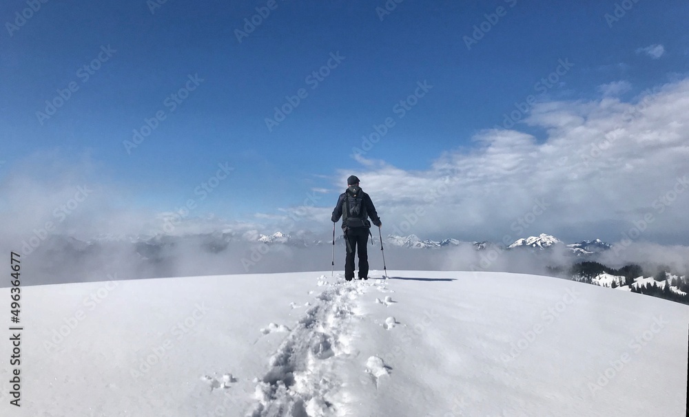 Bergwanderer (männlich) mit Rucksack und Stöcken von hinten im Winter mit Spuren im Schnee