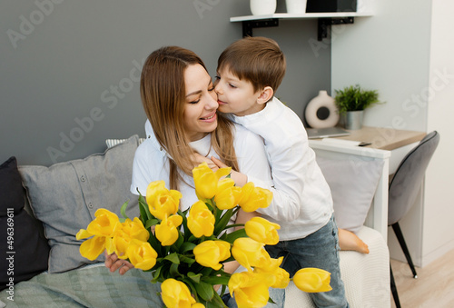 mom and son in a room on a gray background with yellow flowers smile and rejoice in spring.
