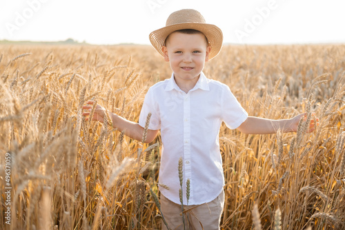 cute smiling child boy in straw hat in wheat field on summer sunset.