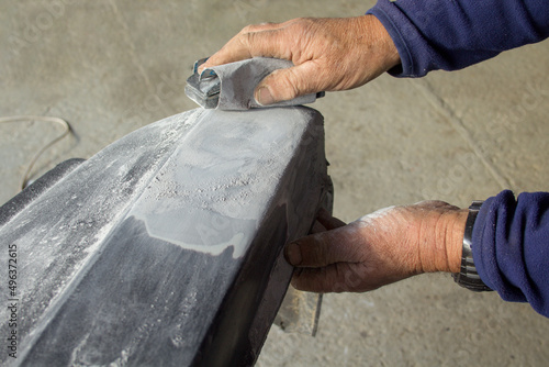 Image of the hands of a body shop plastering and sanding the bumper of a car