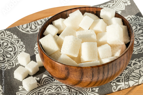 In a wooden dark bowl lies sweet lump sugar in the form of cubes. 