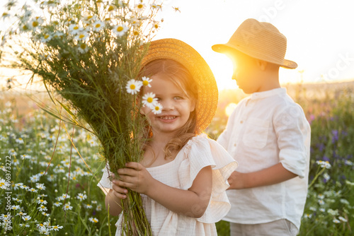 happy child boy and girl in straw hats holds bouquet of field chamomile on sunset summer photo