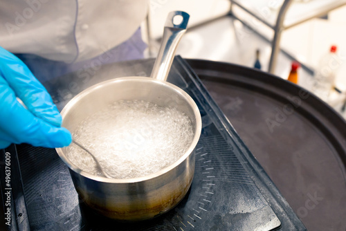 boiling water in a ladle on the stove, a gloved hand stirs the water with a spoon