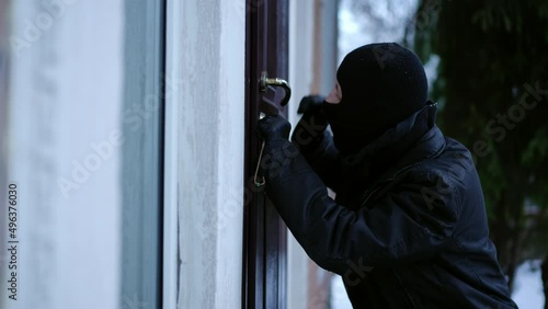 Side view thief picking lock entering empty house on winter day. Caucasian young man in ski mask breaking in private property. Illegal actions and law violation photo