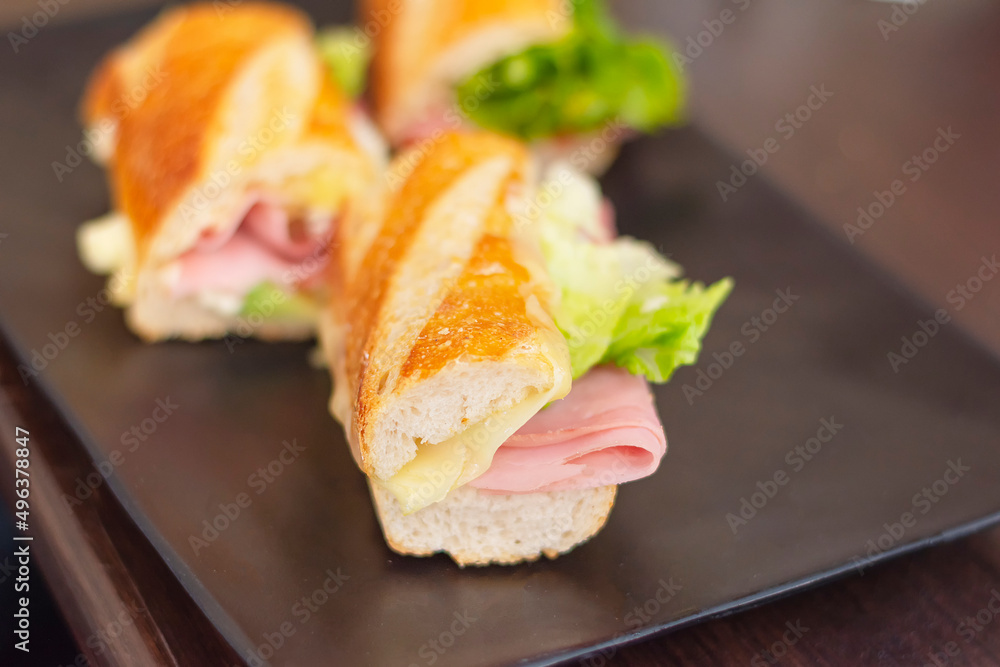 delicious ham sandwich with cheese and lettuce, on a black plate, cooked in a restaurant