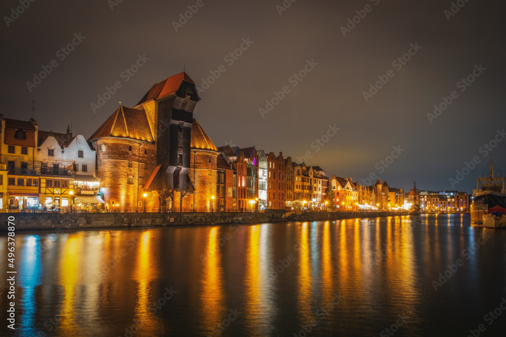 Beautiful architecture of the old town in Gdansk by the Motlawa river with a historic port crane at night. Poland, November 2021