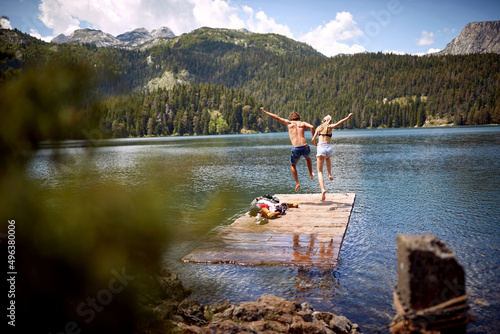A young couple is jumping into the lake during mountain hiking on a beautiful day. Trip, nature, hiking