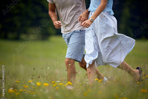 Couple holding hands and running in green meadow. Joyful couple in nature. Fun, togetherness, lifestyle, nature concept.