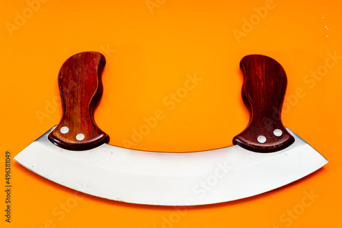 Mezzaluna knife with stainless steel blade and wooden handles insulated on orange background. photo