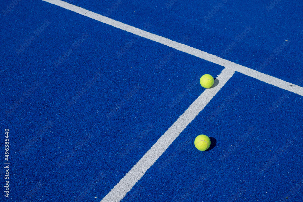 two balls near the center line on a blue paddle tennis court