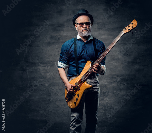 Cool elderly hipster guitarist playing guitar against dark background