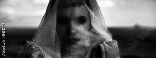 Dark creepy portrait of young woman with hollow eyes wearing veil in black and white	
