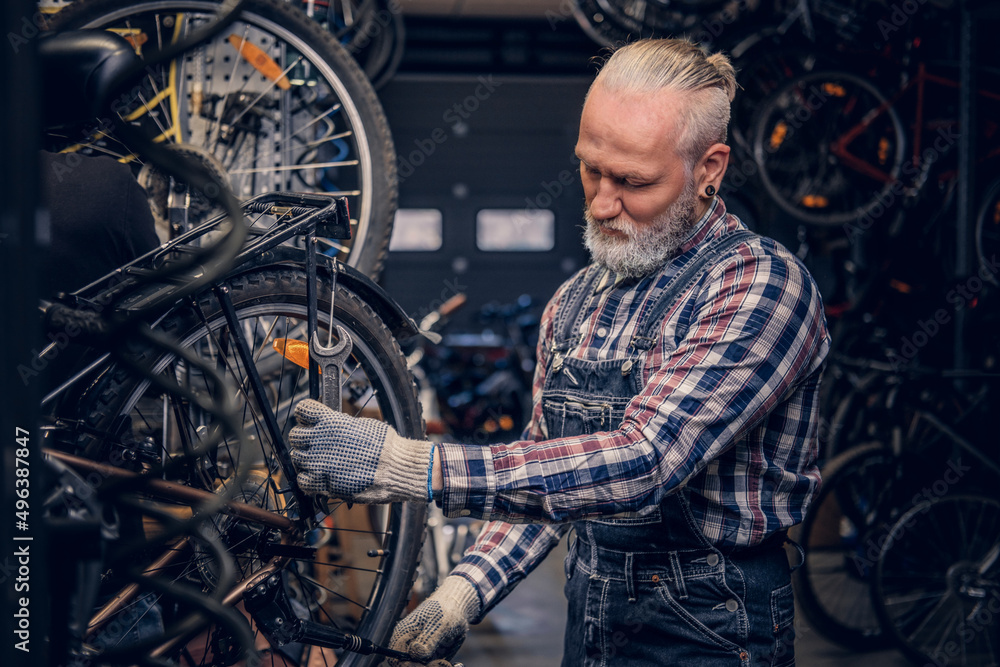 Elderly handyman dressed in plaid shirt and overalls around bikes