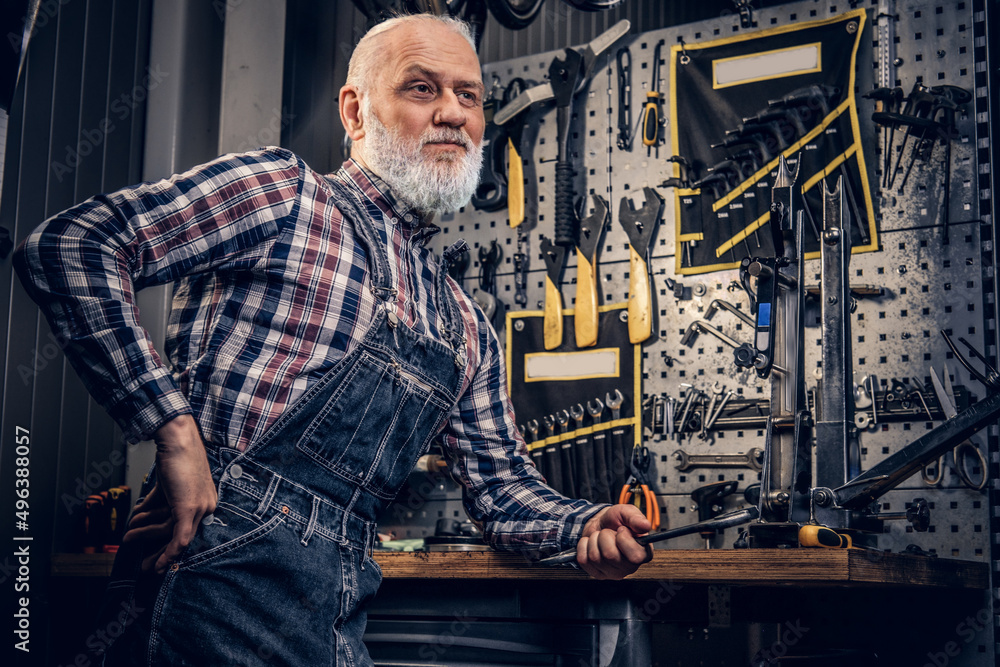 Elderly repairman with gray beard leaning workbench in repair shop Elderly repairman with gray beard leaning workbench in repair shop