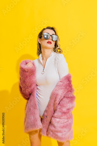Gorgeous young woman posing in luxurious fur coat and bodysuit. Fashion, beauty. Studio shot.