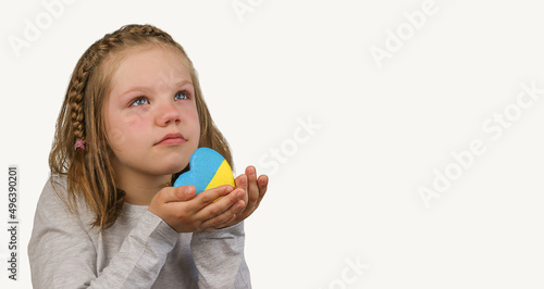 The little girl calls to Stop war, holding heart in the colors of the flag of Ukraine. Ukrainian flag heart. Grey background. Copy Space. No war. Stop war.