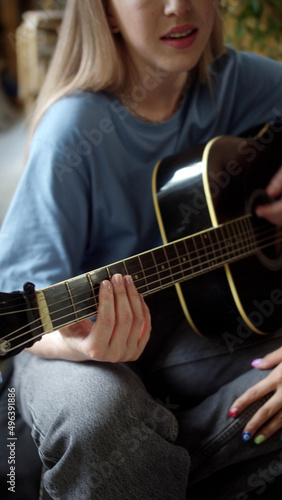 Two lgbt girls are sitting in the lining room on the sofa, playing guitar and singing songs