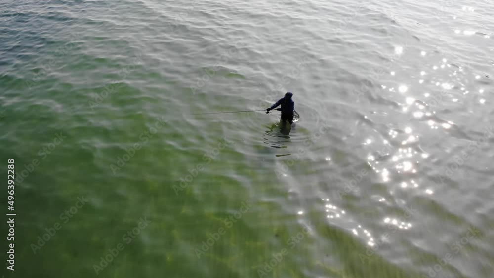Luftaufnahme von Angler mit Angel in Wathose im Wasser bei Sonne watend per Drohne mit Schwenk gefilmt Luftaufnahme von Angler mit Angel in Wathose im Wasser bei Sonne watend per Drohne mit Schwenk gefilmt