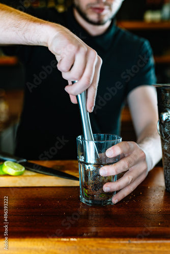 detail of the hands of a young and modern waiter  crushing the mojito ingredients to release their juices . vertical