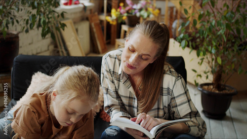 A woman studies what a child is drawing and looks in her notebook