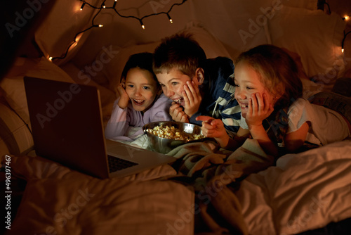 Kids are never far from technology. Shot of three young children using a laptop in a blanket fort.