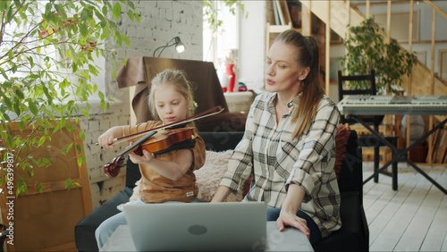Mom and her daughter are engaged in the violin with a tutor. They use a computer