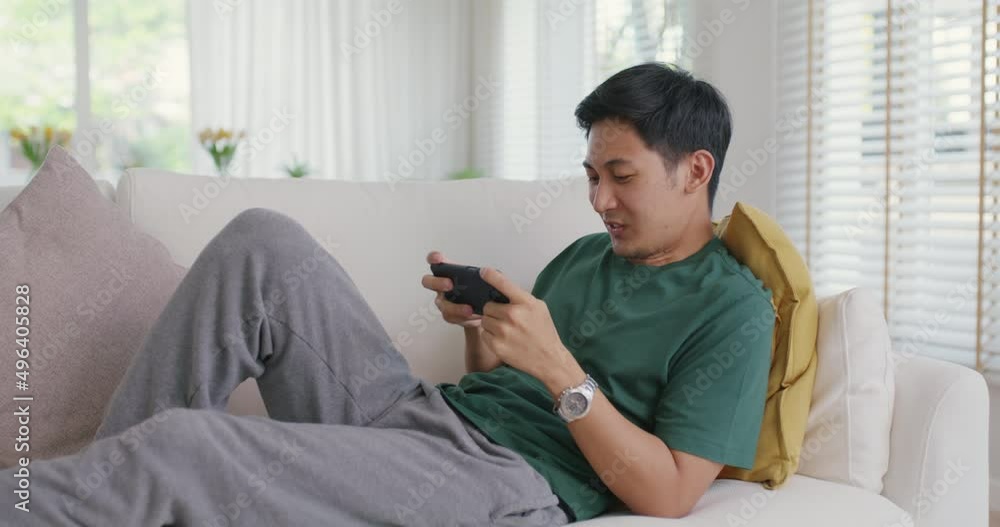 Asia people young man relax sitting easy at home sofa couch laugh smile enjoy play video game social media on mobile app, win online stream casino battle trade, leisure teen activity happy fun joy. Asia people young man relax sitting easy at home sofa couch laugh smile enjoy play video game social media on mobile app, win online stream casino battle trade, leisure teen activity happy fun joy.