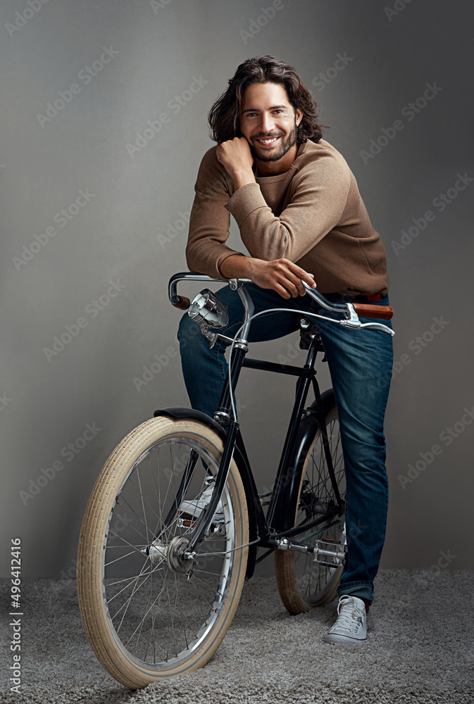 Obraz premium The hippest way to get around. Studio shot of a handsome young man leaning against a bicycle in front of a gray background.