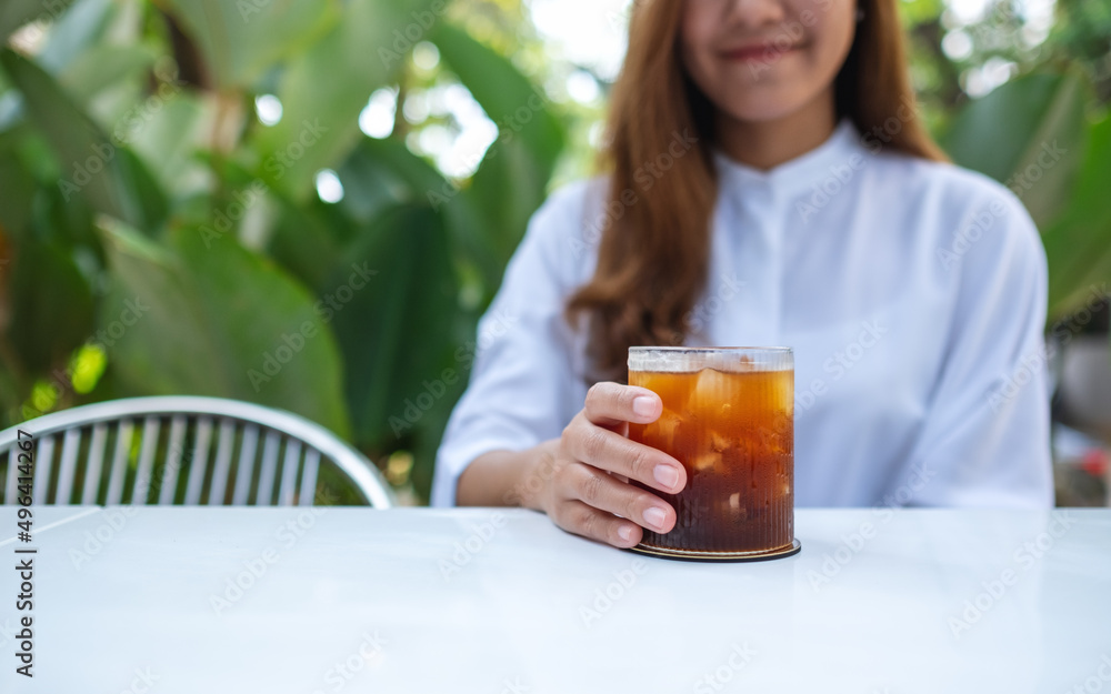 Closeup image a young woman holding and drinking iced coffee in the outdoors Closeup image a young woman holding and drinking iced coffee in the outdoors