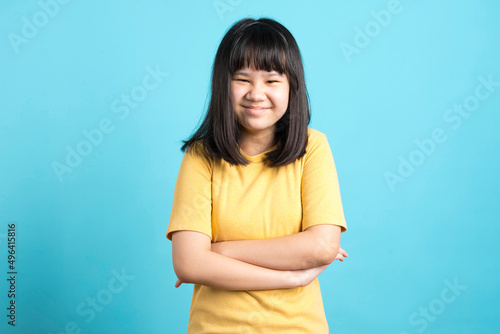 Cute Asian girl in yellow shirt laugh and standing on blue background.