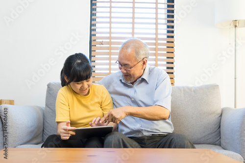 Old senior asian grandparent play and watch computer tablet with grandchildren girl at home. Bonding relationship in family.