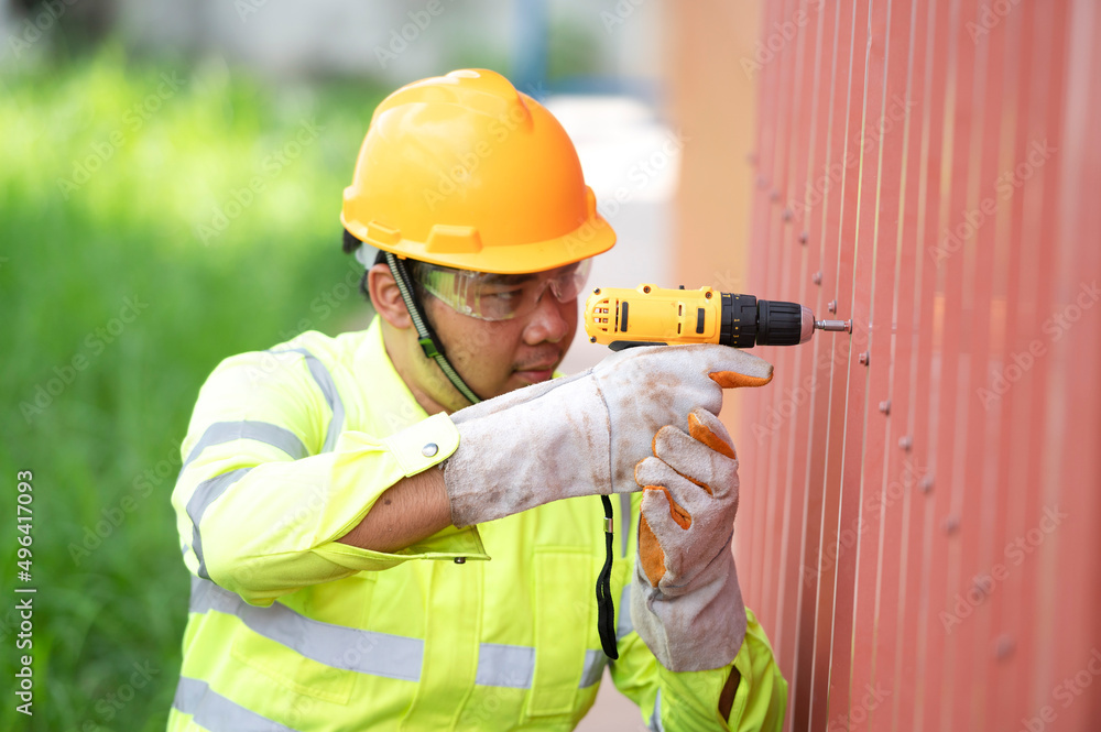 Caucasian construction worker working with a cordless electric screwdriver on a steel fence,cordless drill Caucasian construction worker working with a cordless electric screwdriver on a steel fence,cordless drill