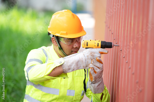 Caucasian construction worker working with a cordless electric screwdriver on a steel fence,cordless drill