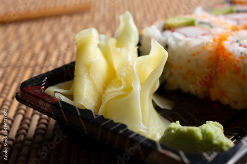 Obraz na plátně A closeup view of a pile of pickled ginger with some wasabi, on a tray of cut roll sushi